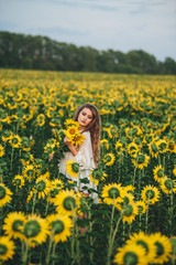 Fototapeta na wymiar Young beautiful woman in a dress among blooming sunflowers. Agro-culture.
