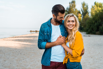 Naklejka premium happy young couple hugging and walking on sandy beach