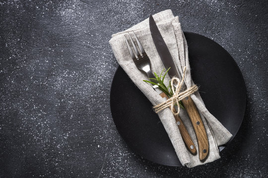 Black plate, cutlery and napkin on stone table top view.