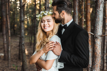 handsome groom hugging beautiful bride with closed eyes in forest