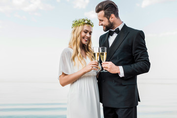smiling wedding couple clinking with glasses of champagne on beach