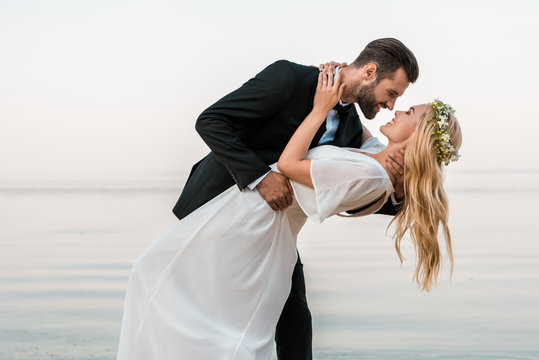 affectionate wedding couple going to kiss on beach