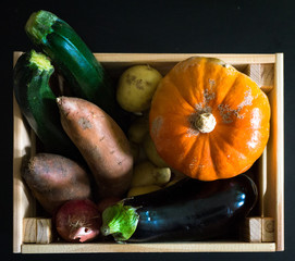 Flat lay of a wooden crate showing seasonal vegetables in a dark background