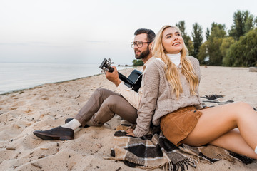 handsome boyfriend in autumn outfit playing acoustic guitar for smiling girlfriend on beach