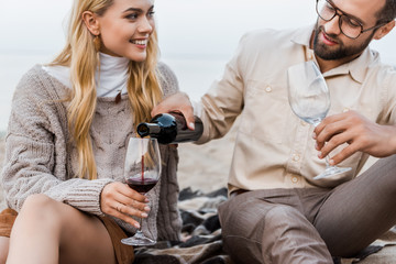 boyfriend in autumn outfit pouring red wine into glasses on beach