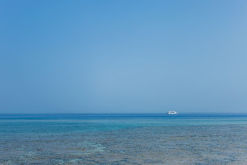 White ship in distance. Blue marine water and clear sky background. Horizontal color photography.