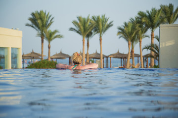 View from back of white european tourist swimming in blue water of outdoor pool at tropical hotel resort. Only head over waterline and body underwater. Horizontal color photography.