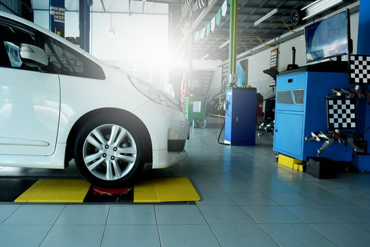 the white car awaiting on position during wheel alignment at the car repair shop