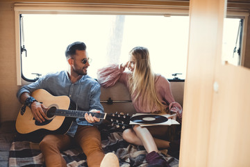 Obraz na płótnie Canvas musician playing on acoustic guitar while girl looking at him and holding vinyl record inside campervan