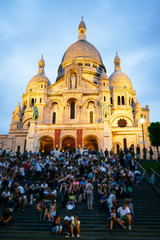 People on stairs on the hillside of Montmartre in front of the Sacre Coeur Basilica.