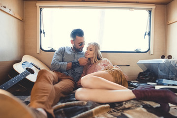 hippie couple hugging inside campervan with acoustic guitar and vinyl player
