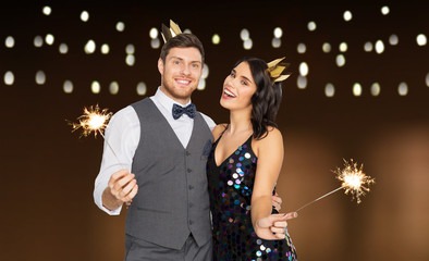 celebration, fun and holidays concept - happy couple with crowns and sparklers at party over garland lights background © Syda Productions