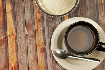 A cup of black coffee, a plate of pastry, and a bowl of sugar on a brown wooden background