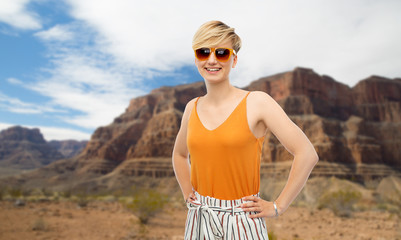 travel, tourism and summer holidays concept - happy smiling young woman in sunglasses over grand canyon national park background