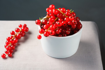 Red currants in a white porcelain bowl. Gray linen table, high resolution