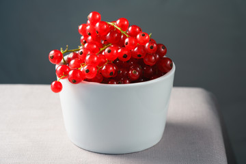 Red currants in a white porcelain bowl. Gray linen table, high resolution