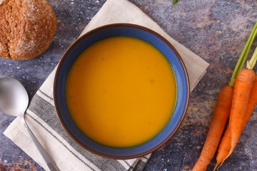 Bowl of carrot soup with a bread roll and carrots