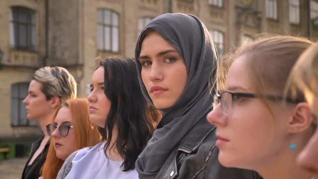 Gorgeous caucasian girl in hijab looks precisely from group of various women outdoor