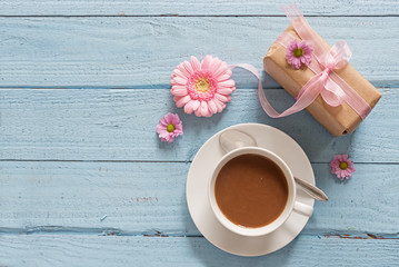 Coffee cup, pink flowers and a gift on pastel blue wood background with copy space, breakfast with love on Valentines or Mother's Day, top view from above
