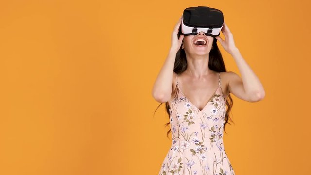 Beautiful young woman experiencing VR virtual reality for the first time. She is very amased. Isolated over yellow orange background