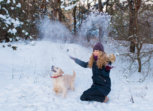 young woman plaing with golden retriever on winter walk.