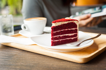 The red velvet cake is placed on a white plate on a wooden tray,Cappucino coffee put on wooden tray