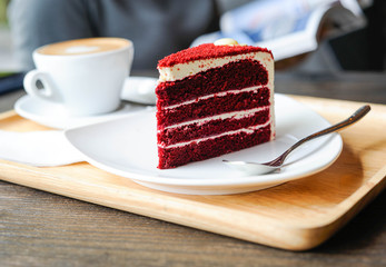 The red velvet cake is placed on a white plate on a wooden tray