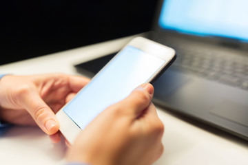 business, deadline and technology concept - close up of businesswoman hands with smartphone and laptop computer working at night office
