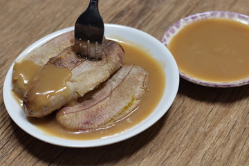 Grilled banana with dipping sauce on wooden table.