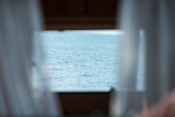 view of blue sea from trailer window with curtains