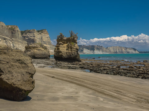 Giant boulders and sheer cliffs rise above the rocky beach at Cape Kidnappers on a beautiful sunny day at Hawke&rsquo;s Bay in New Zealand
