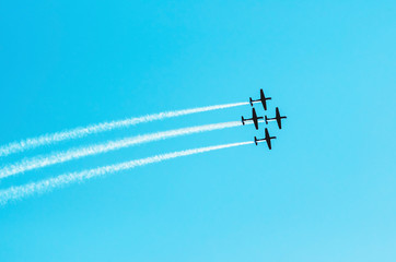 Squad of four airplanes flying together leaving a smoke trail behind. Aerial acrobatics airplanes. Clear blue sky day.