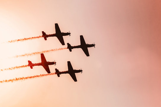 Squad of four airplanes flying together leaving a smoke trail behind, photo at a sunset. Warm colours. Space for text on sky.