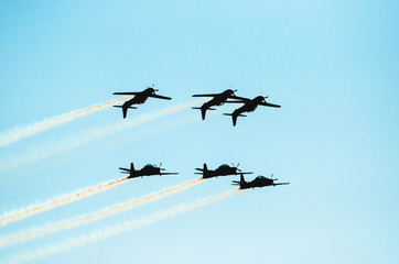 Three planes flying upside down and others three flying normally under. Squad flying together, smoke trail behind. Planes making aerial acrobatics. Clear blue sky day. 