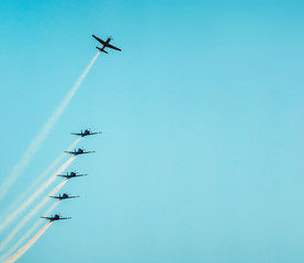 Airplane flying up separating from the squad. Airplanes flying together leaving a smoke trail behind. Aerial acrobatics airplanes. Clear blue sky day. Large space for text. - obrazy, fototapety, plakaty