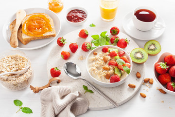healthy breakfast with oatmeal porridge, strawberry, nuts, toast, jam and tea