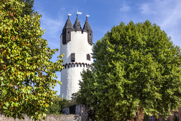 Germany, Rhine-Main area, Hanau, Steinheim: Famous white donjon tower in the green castle park of the German town with flags, old vintage city wall, trees and blue sky - concept travel architecture