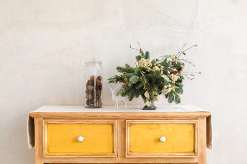 Christmas decorations and conifer twigs placed on dresser with yellow drawers on background of...