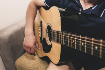 Man at home is playing the guitar. Guys hands are taking the chord on strings. Music making...