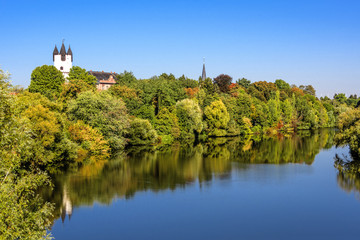 Fototapeta na wymiar Germany, Rhine Main area, Hanau, Steinheim: Reflection of green castle park of the German town with famous white donjon tower, roof top of mansion, calm Main river, trees and blue sky in background.