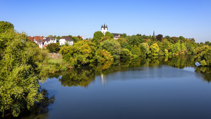 Fototapeta na wymiar Germany, Rhine Main area, Hanau, Steinheim: Reflection of skyline in calm Main river with green castle park, famous donjon, white tower, roof top of mansion, museum, trees and blue sky in background.