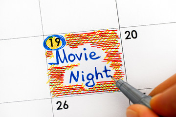 Woman hand with pen writing reminder Movie Night in calendar.
