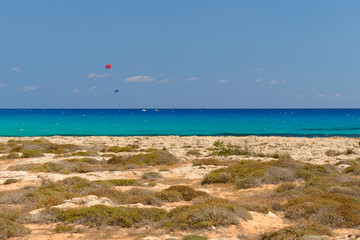 Two parachutists tied to boats skate in the turquoise sea