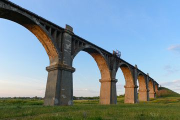 Fototapeta premium old arched railroad bridge in the green field at sunset