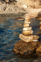 Fototapeta na wymiar Pile of pebbles on the sea front on a beautiful day. Pebble stack on the seashore. Stone pyramid. Balanced Zen stones.