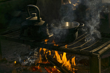 a pot and a kettle stand over a fire on a portable hearth made of metal rods in a nomad's dwelling..