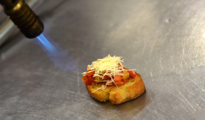 Schmelzen von Käse auf Bruscetta mit blauer Flamme aus dem Küchenbrenner 