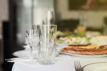 Glasses goblets on white table. Room with table serving fruits and dishes and meal.