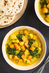 Homemade Indian vegetarian cauliflower pumpkin and spinach curry in bowls, fresh homemade naan bread on the side, photographed overhead on slate (Selective Focus, Focus on the dish)