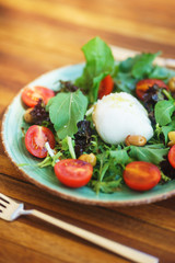 Mozzarella with cherry tomatoes with arugula and olives in a plate on a wooden table. 